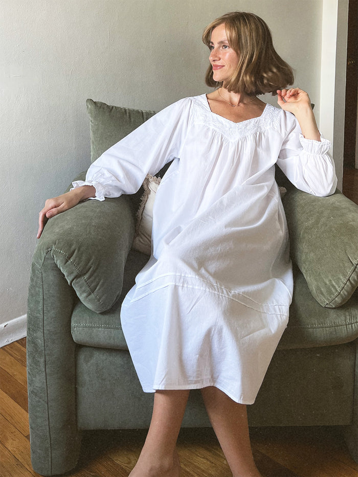 Woman wearing a white nightgown sitting on a green couch.