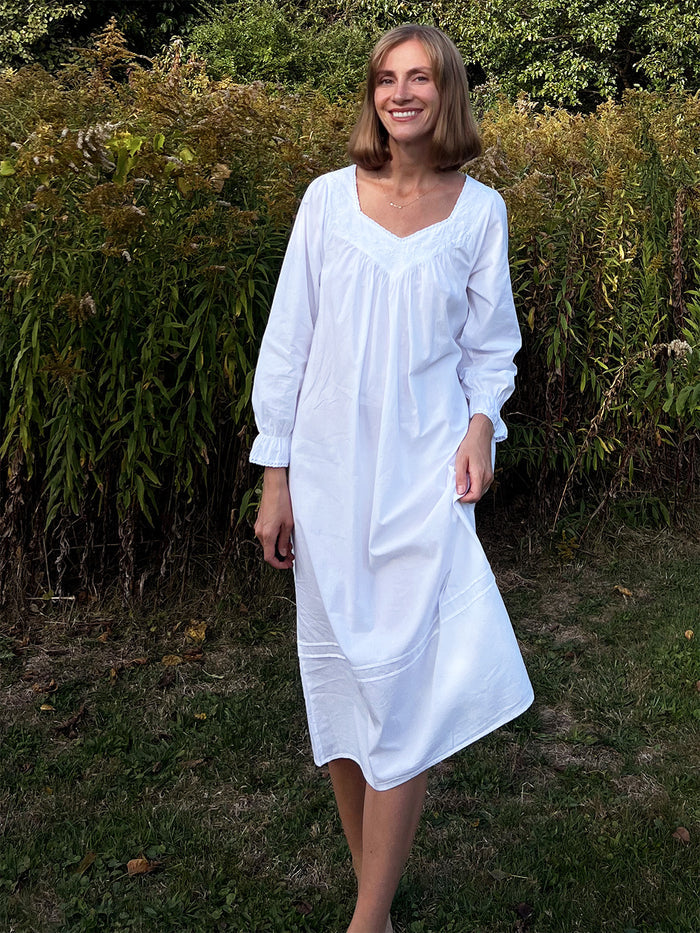 Woman wearing a white dress standing in front of greenery