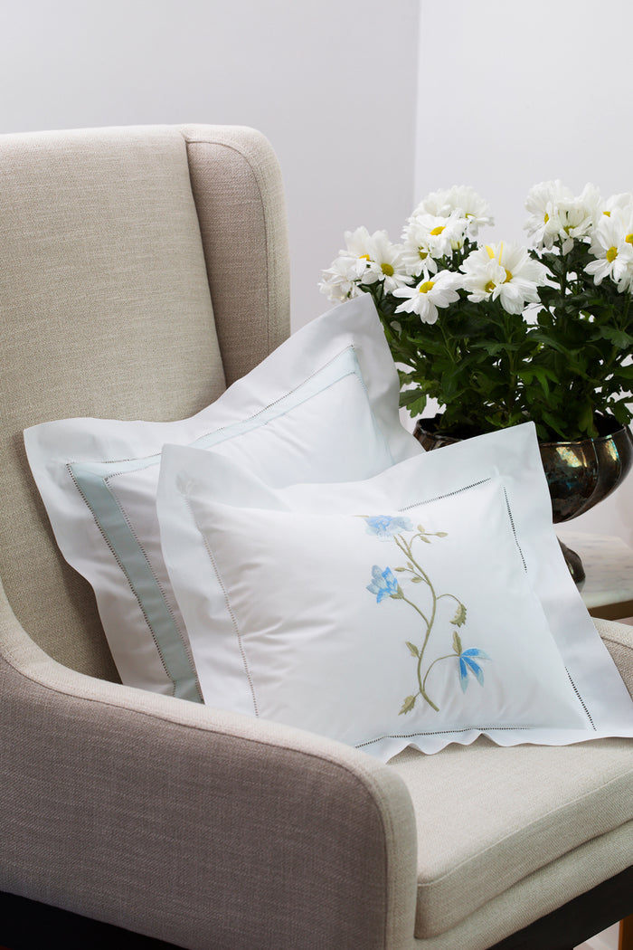 Decorative pillows with floral embroidery on a beige armchair with a vase of flowers in the background.