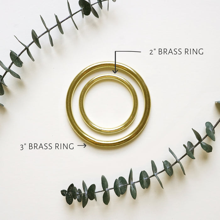 Two brass rings, one labeled as 2 inch and the other as 3 inch, placed on a surface with a decorative element in the background.
