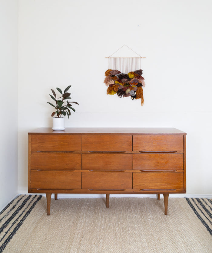 Minimalist interior featuring Cedarville textile wall hanging above mid-century dresser — handcrafted mixed-media wall decor in warm autumn palette.