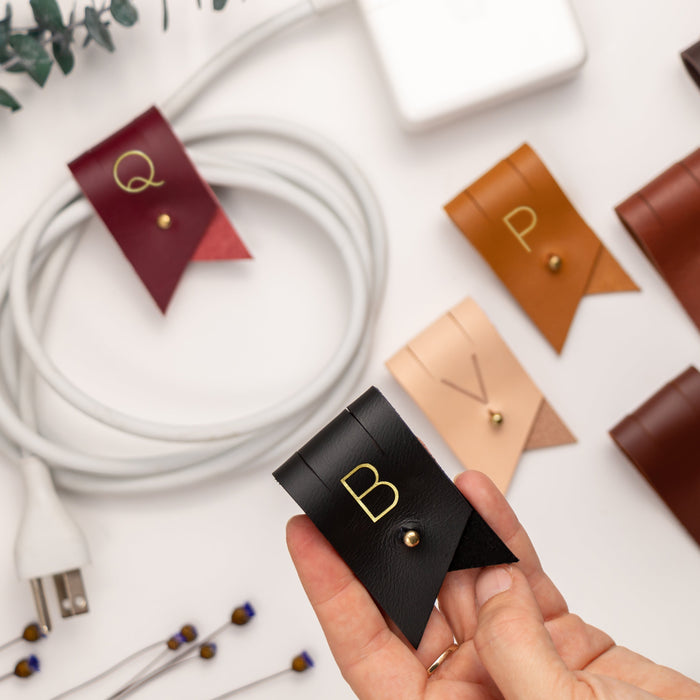 Custom letter leather cable organizers in Wine, Black, Veg Tan, Nicotine and rich brown Keyaiira colors, designed for charger cords, earbuds, electronics and portable cable storage