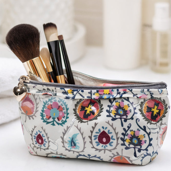 Makeup bag with floral pattern containing makeup brushes on a light background