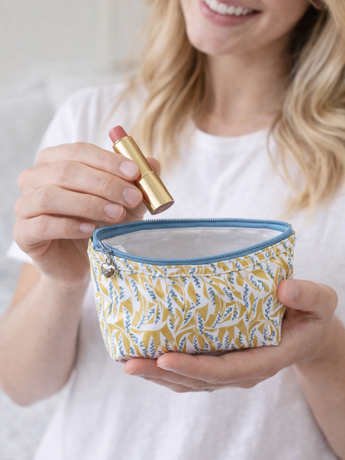 Woman holding a small yellow fabric pouch with a blue zipper and a gold lipstick.