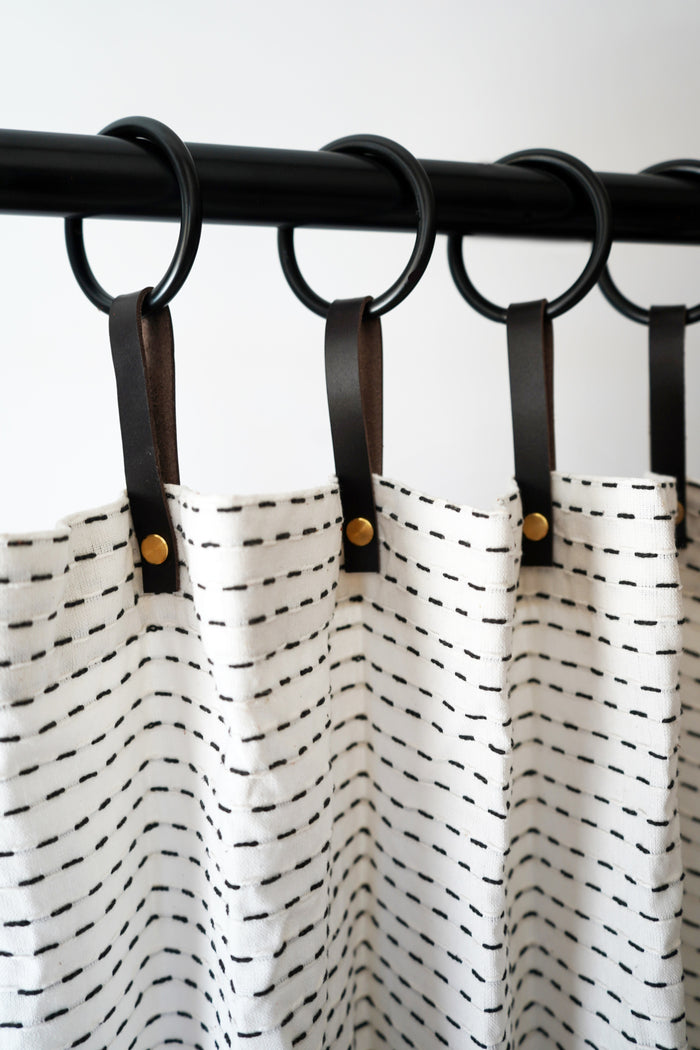 Row of chocolate leather shower curtain hangers with black metal rings securing a patterned shower curtain on a matte black rod, creating a clean, cohesive look for modern bathroom interiors.