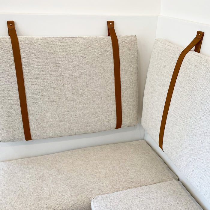 Close-up of tan standard width leather wall strap holding bench cushion — vegetable-tanned leather wall anchor detail with clean, tailored interior finish.