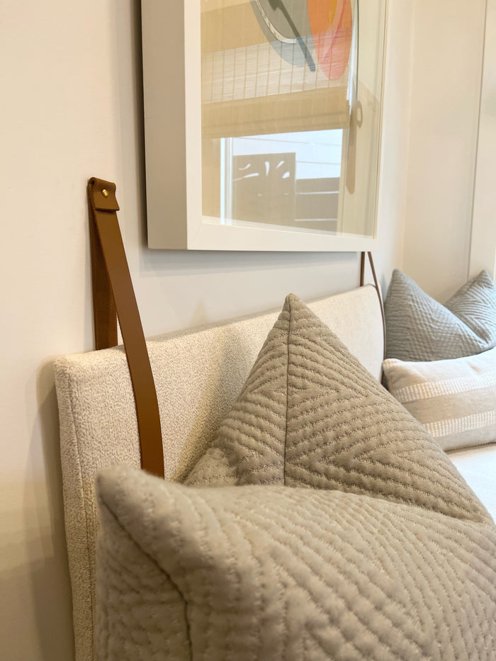 Keyaiira custom leather wall strap securing a cushion to a sofa — handcrafted leather hardware detail in warm brown with brass screw.