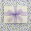 Gift box with a purple ribbon on a lavender patterned background