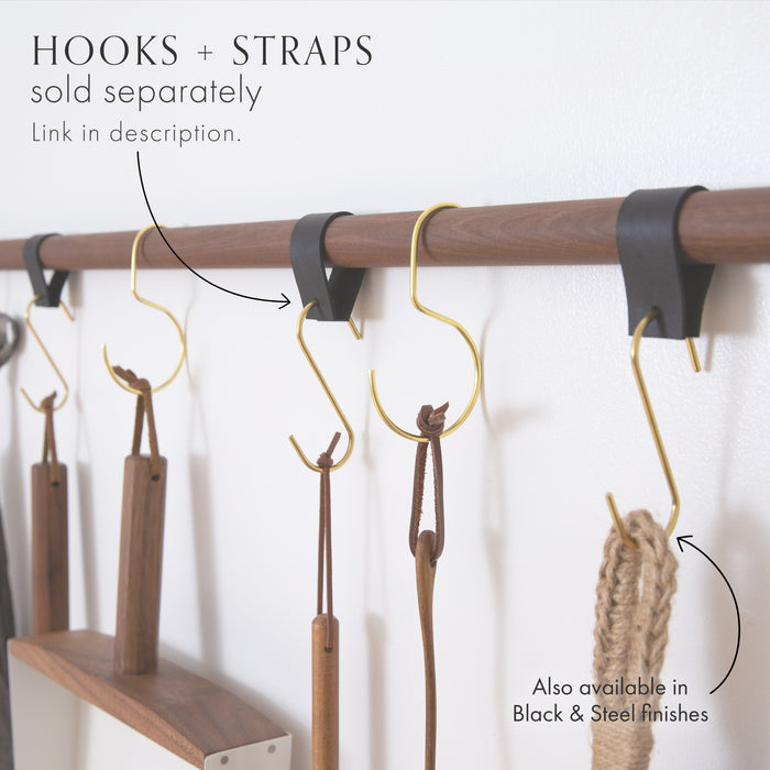 Close-up of Keyaiira leather straps on wood dowel with brass S-hooks holding kitchen utensils — modular leather wall rail system for organized storage.