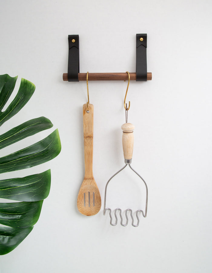 Keyaiira leather strap wall rail with wood dowel holding wooden kitchen tools — modern leather and wood wall storage solution.