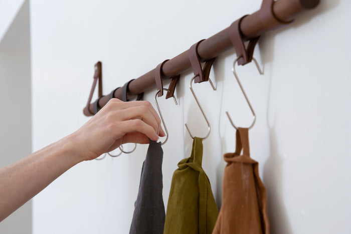 Leather hanging loops paired with metal hooks on wood rail — minimalist wall organization system designed for kitchens, entryways, and utility spaces.
