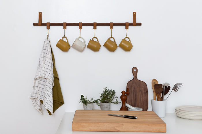 Wall-mounted wood rail with hooks and hanging kitchen tools — minimalist kitchen organization with warm natural materials.