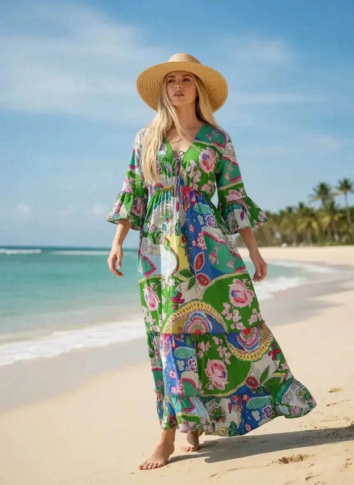 Woman in a colorful dress and hat standing on a beach with palm trees in the background