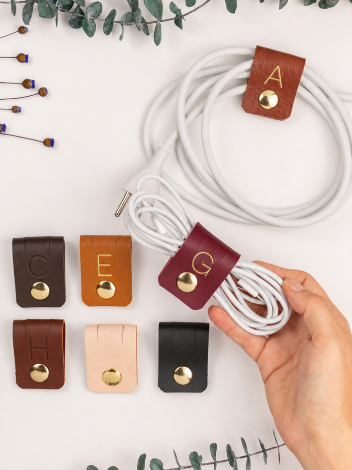 Personalized initial leather cord holders in assorted Keyaiira colors, designed for charging cables, USB cords, computer accessories, electronics and convenient cable management