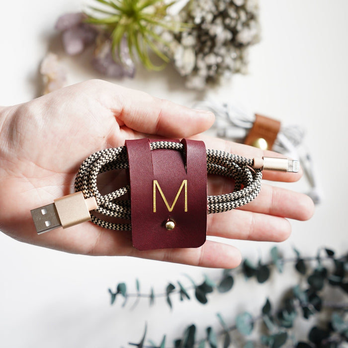 Handcrafted Wine leather large cable holder with M initial, Stud & Post closure securing a braided USB charging cord for cable management, electronics storage and organized workspaces by Keyaiira