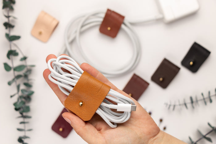 Handcrafted Cognac leather cable wrap securing a coiled white charging cord, reusable large cord organizer with Stud & Post hardware for desk, home office and travel organization by Keyaiira
