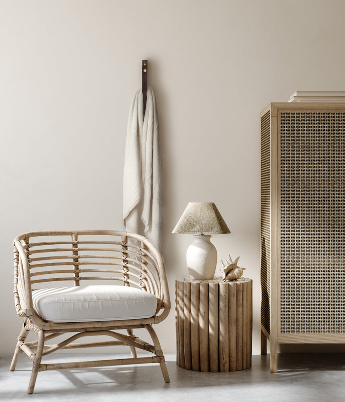 Chocolate leather wall strap with brass snap hardware styled in a warm neutral living space, holding a draped throw beside natural rattan furniture, highlighting Keyaiira’s handcrafted modern-rustic wall organization.