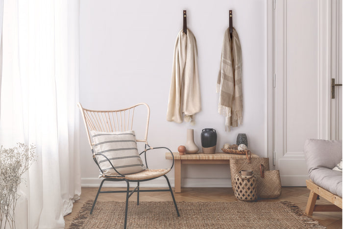 Chocolate colored leather wall straps with brass snap hardware hanging textured throws in a bright bedroom, demonstrating Keyaiira’s functional and decorative hanging solution for blankets, towels, or robes.