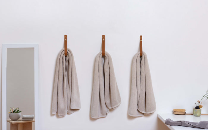 Set of three Nicotine colored leather wall straps with brass hardware mounted evenly across a white wall, displaying a coordinated minimalist hanging system for blankets, towels, and textiles.