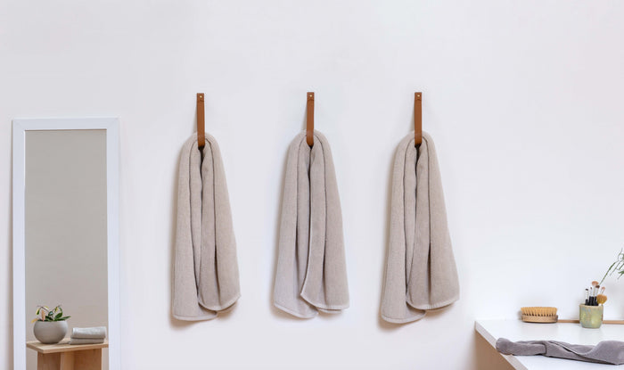 Set of three large leather wall straps in nicotine brown used for hanging neutral towels in a minimalist bathroom.