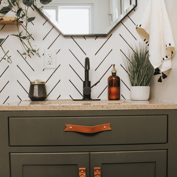 Keyaiira cognac leather cabinet handle with brass hardware installed on dark bathroom vanity drawer, modern minimalist leather drawer pull for bathroom renovation.