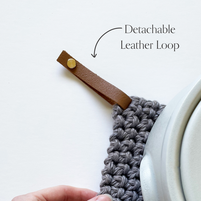 Keyaiira detachable leather hanging loop attached to a knit potholder, highlighting the removable leather loop feature with brass screw.