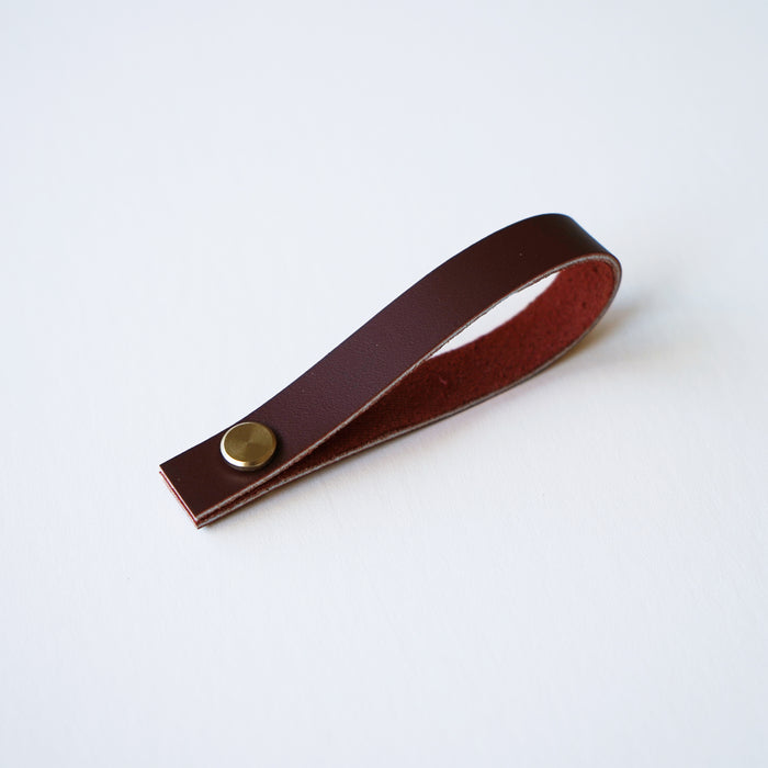 Wine colored leather hanging loop with brass hardware on white background minimalist leather hanging loop by Keyaiira.