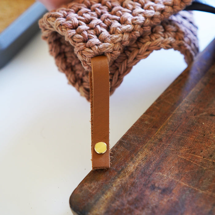 Detachable leather hanging loop holding a knit potholder over a wooden counter edge — handcrafted Keyaiira leather loop.
