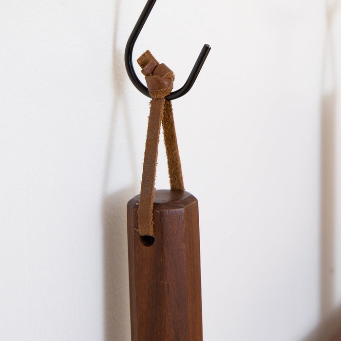 Close-up of a detachable Keyaiira leather hanging loop tied around a wooden kitchen tool handle and hung on a wall hook handcrafted leather loop with brass hardware for kitchen organization.