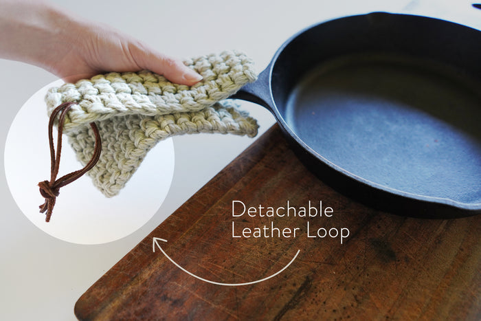 Detachable leather hanging strings by Keyaiira attached to a crocheted knit potholder and shown near cookware handcrafted leather hanging strings for organizing kitchen textiles.