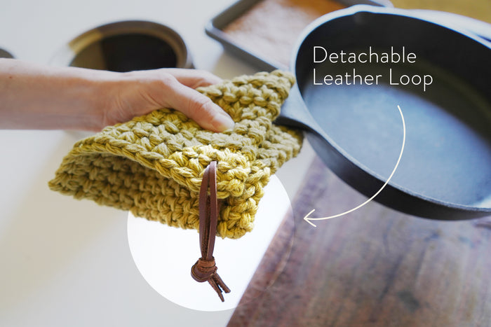 Detachable leather hanging strings by Keyaiira holding a green crocheted knit potholder over a counter edge — handcrafted leather hanging strings for functional kitchen storage.