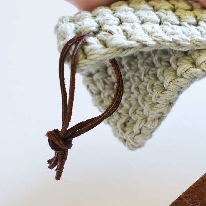 Hand holding a crocheted knit square with detachable leather hanging strings by Keyaiira — handmade leather hanging strings shown in use.