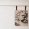 A rectangular canvas wall art print featuring a monochrome landscape painting of trees and water, hanging from two brown leather straps on a brass rod against a white wall by keyaiira.