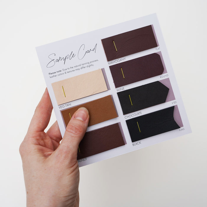 Keyaiira Leather Sample Card hand selecting a black leather swatch from color options including veg-tan, mahogany, and wine. Natural vegetable-tanned leather color samples for custom handmade hardware.