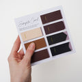 Keyaiira Leather Sample Card hand selecting a black leather swatch from color options including veg-tan, mahogany, and wine. Natural vegetable-tanned leather color samples for custom handmade hardware.