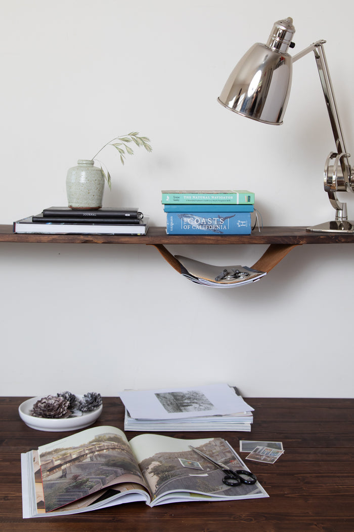 Keyaiira Leather Sling shown in use as an under-shelf storage holder for stationery and letters — handcrafted leather wall sling adds functional, minimal organization to a wooden shelf. Wood shelf not included.