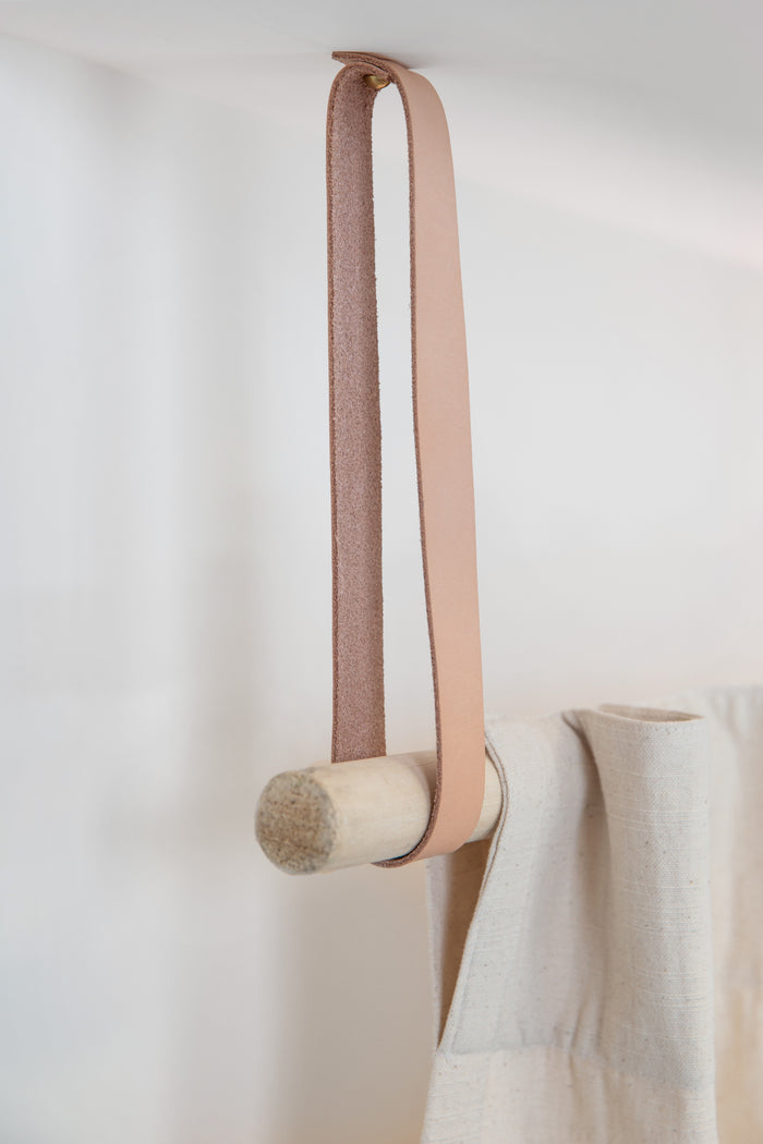 Close-up of leather ceiling strap with wooden dowel detail, showcasing clean hardware and modern hanging system for shelves or rods