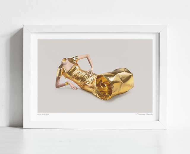 Lose Your Head art print framed horizontal — surreal fashion collage of a headless reclining figure in an extraordinary sculptural gold foil dress catching light with brilliant intensity against a minimal grey backdrop, luxury editorial fashion art for hotel suites boutiques and gallery walls