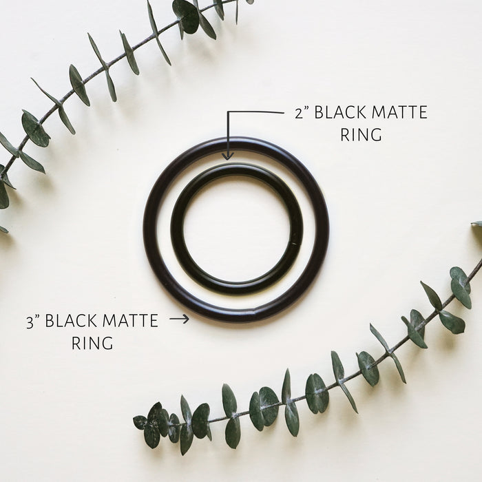 Two black matte rings of different sizes placed on a surface with a plant decoration around them.