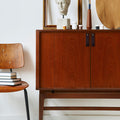 A brown leather pull attached to a wooden furniture piece, with a room setup including a chair and decorative items in the background.