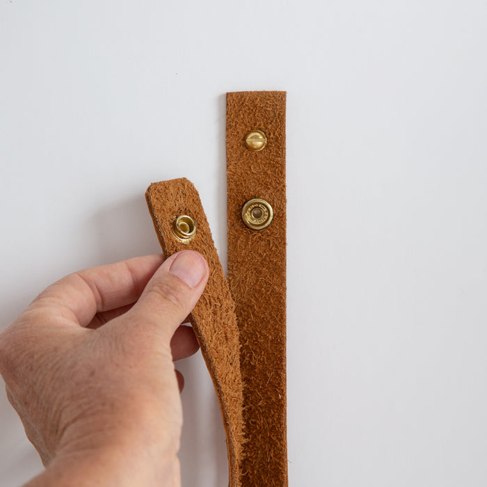 Keyaiira genuine leather wall strap shown in hand, highlighting premium leather thickness and solid brass rivet — handcrafted modern wall hanging loop.