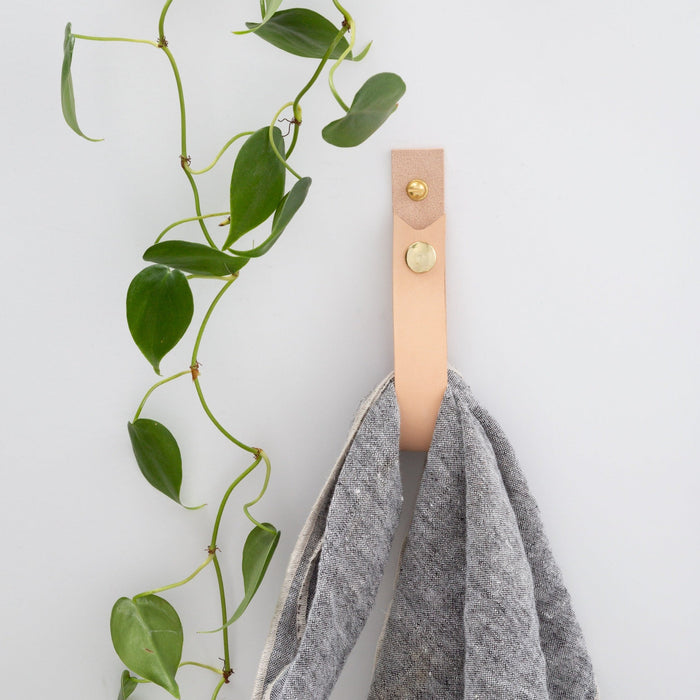 Keyaiira natural leather wall hanging strap with brass rivet holding grey towel — modern bathroom wall hook alternative for minimalist organization.