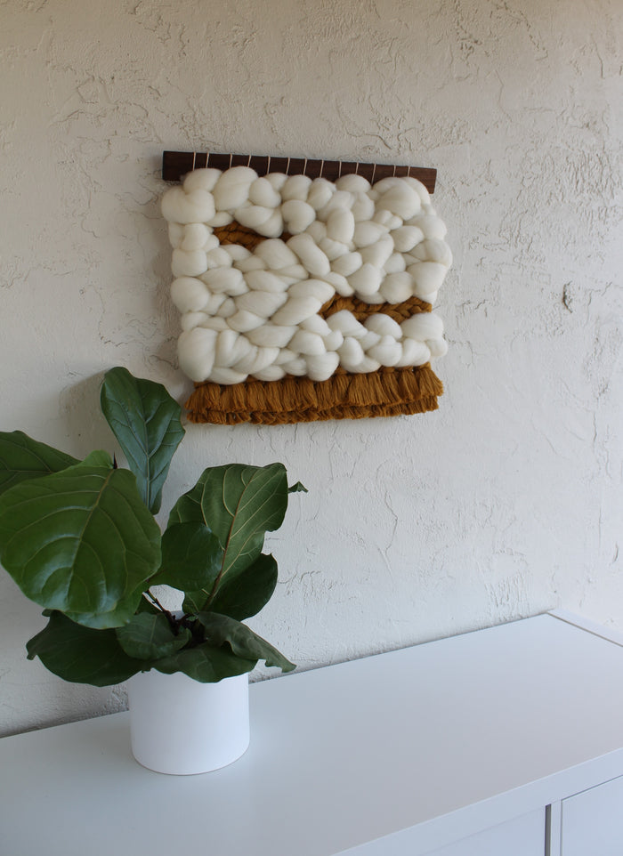 Close-up of Keyaiira handcrafted woven wall art highlighting plush white wool roving and hand-tied brown fringe, emphasizing texture and artisan craftsmanship