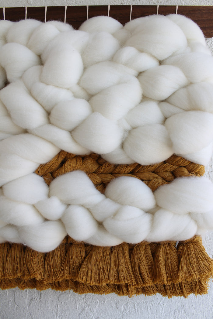 Close-up of Keyaiira handcrafted woven wall hanging showing dense white wool roving and warm brown fringe, emphasizing soft texture and artisan fiber craftsmanship