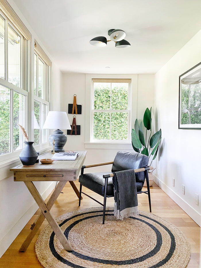 Keyaiira leather display holders styled in a sunlit home office, featuring tan and black artisan leather straps with brass rings used to hang decorative boards on the wall above a wooden desk.