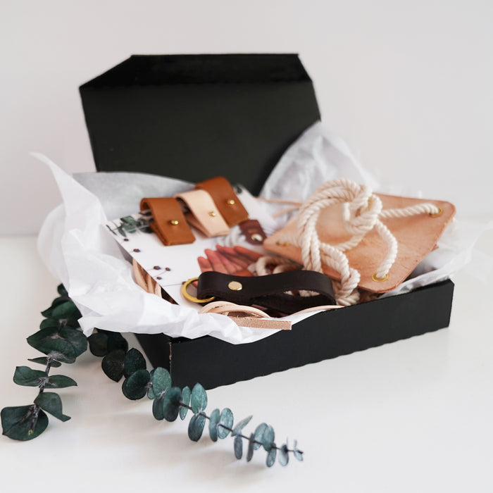 A black mystery box with various home decor items spilling out, including what appears to be a plant hanger, rope, and decorative accessories.