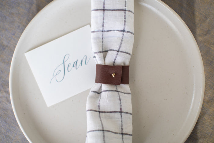 Minimal modern table setting featuring the Keyaiira Leather Napkin Ring in Walnut sleek handcrafted leather holder with brass accent styled with a soft green linen napkin for elevated everyday dining.