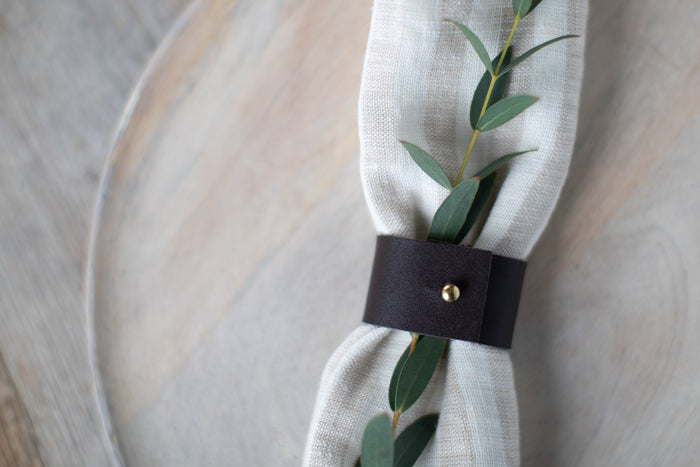Handcrafted Black Leather Napkin Ring by Keyaiira, minimal modern tableware accessory featuring a brass stud accent, shown with a white linen napkin on a clean dining setting for a refined wedding table setting