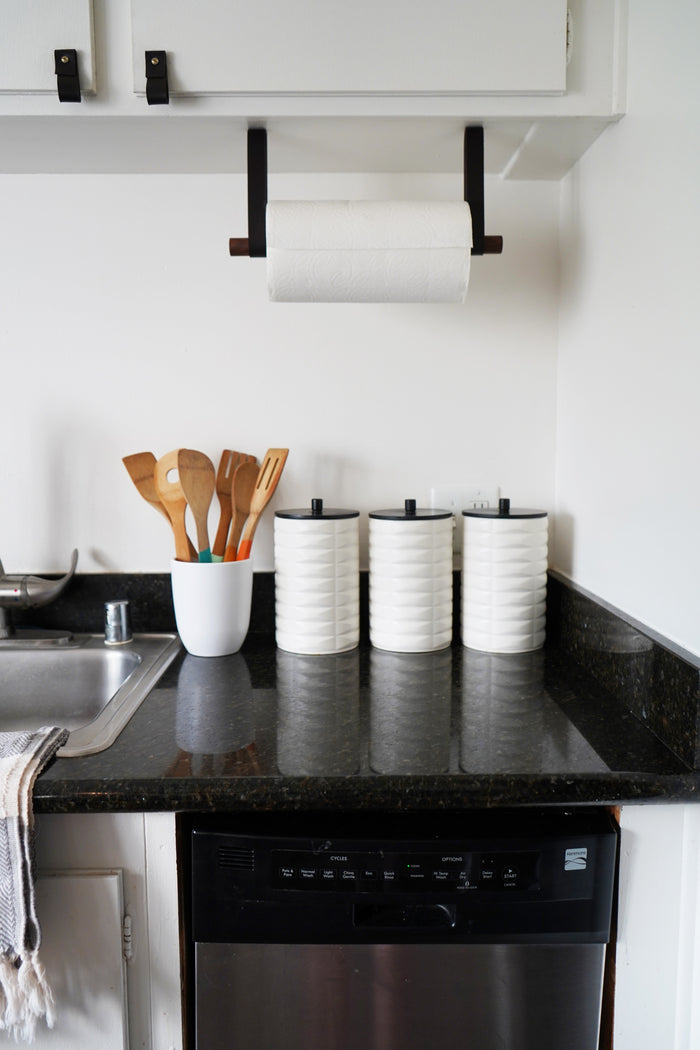 Leather strap paper towel holder mounted above kitchen counter — modern wall-mounted paper roll storage solution.