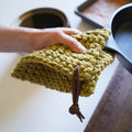 Handwoven cotton potholder with leather cord hanger in olive green — thick textured kitchen hot pad designed for lifting cast iron cookware and protecting countertops.